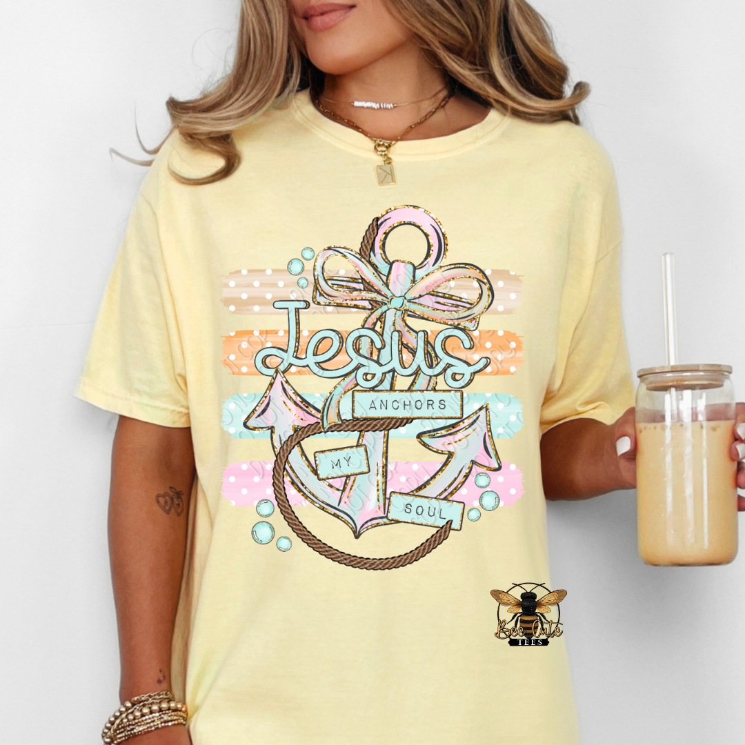 Person wearing a yellow t-shirt with a colorful anchor design and text, holding a drink.