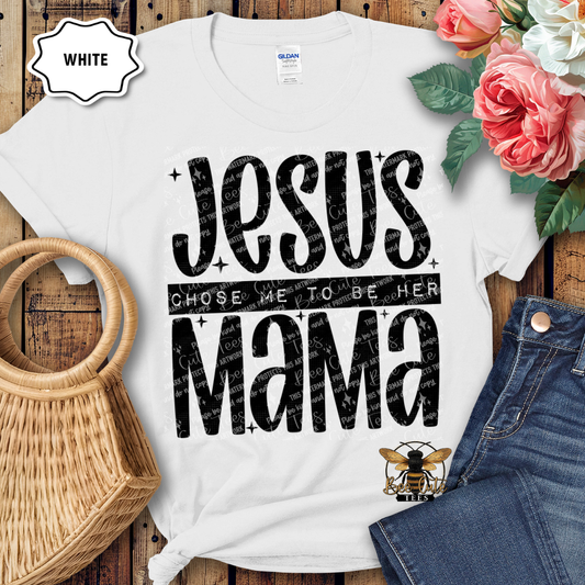 White t-shirt with 'Jesus chose me to be her mama' text on a wooden surface with flowers and jeans.