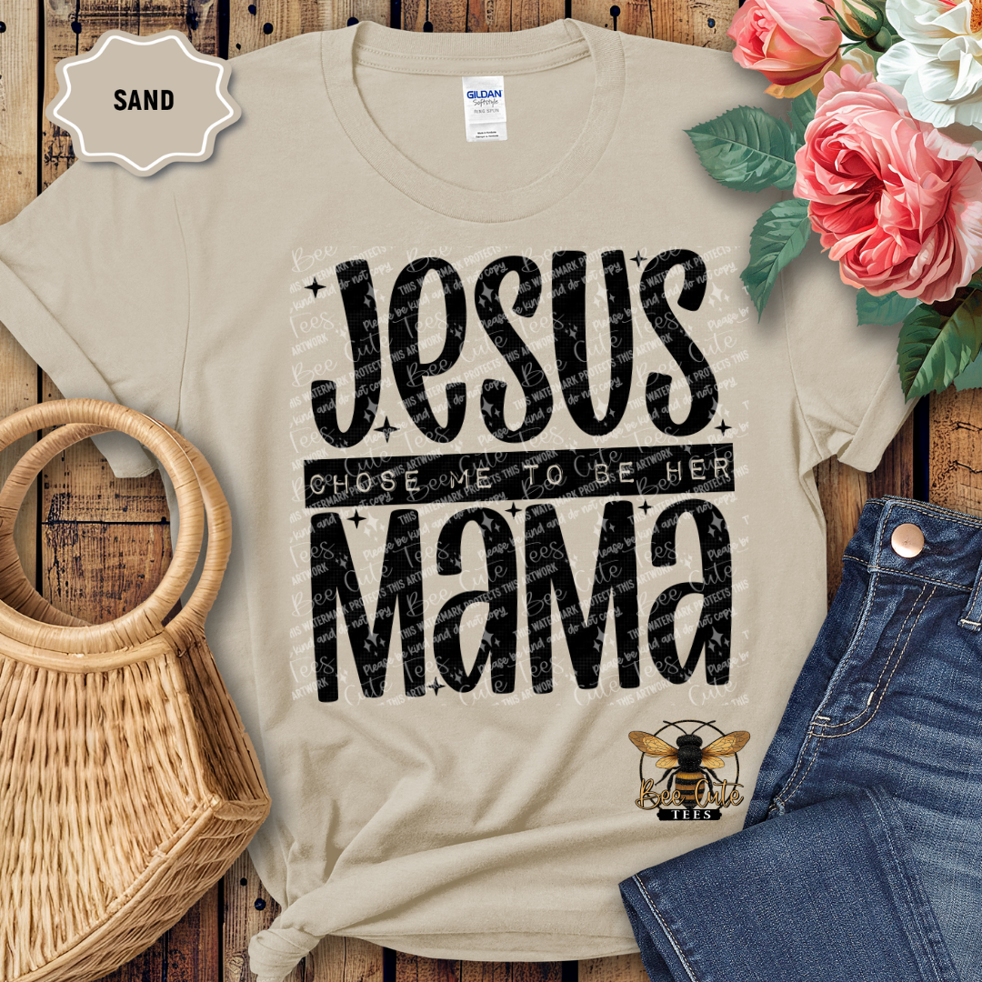 Beige t-shirt with 'Jesus Chose Me to be Her Mama' text on a wooden surface with flowers and jeans.