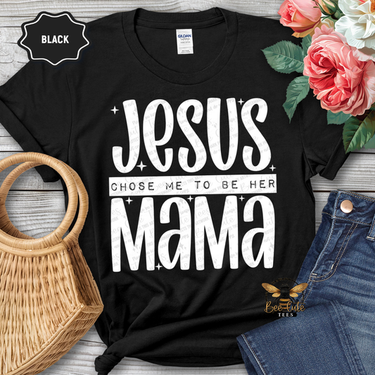 Black t-shirt with 'Jesus Chose Me to Be Her Mama' text, surrounded by flowers and jeans on a wooden surface.