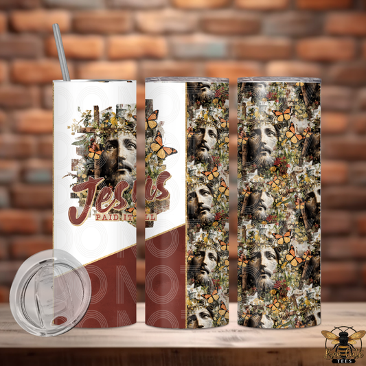 Tumbler with artistic design of faces and butterflies on a wooden surface with a brick wall background.