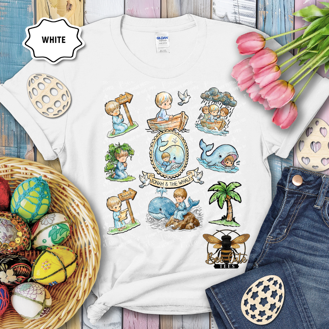 White t-shirt with illustrated designs featuring children, animals, and nature elements, surrounded by Easter decorations.
