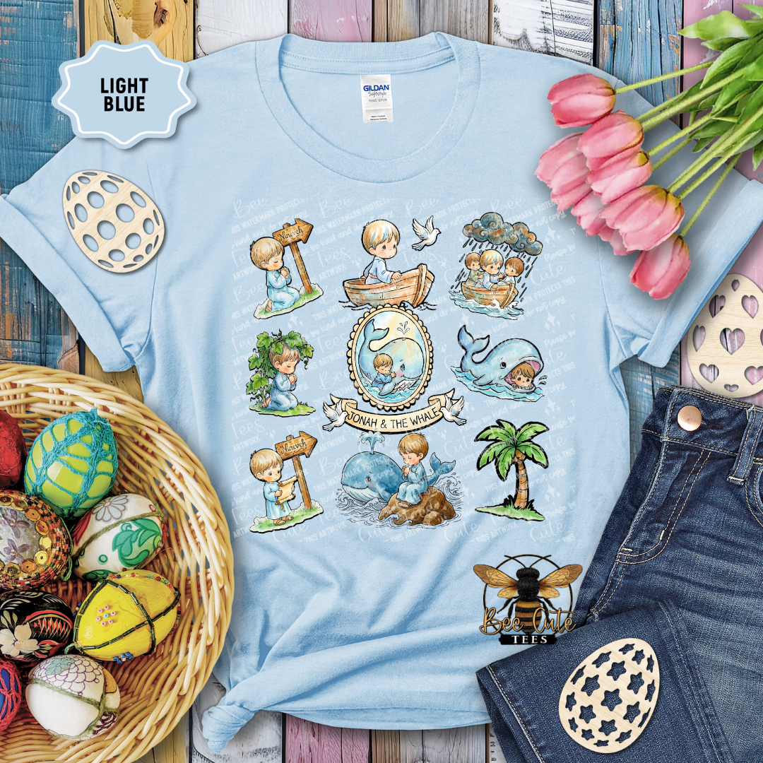 Light blue t-shirt with illustrated designs on a wooden surface with flowers and toys.