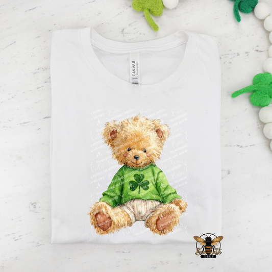 White t-shirt with a teddy bear design wearing a green shirt with shamrock patterns on a white background.