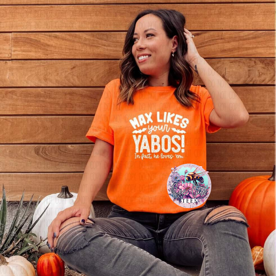 A person wearing an orange t-shirt with the text 'MAX LIKES YOUR YABOS!' on it, sitting in front of a wooden background with pumpkins around.