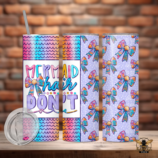 Colorful 20 oz tumbler featuring pastel mermaid-inspired scales, seashell bow designs, and playful text that reads “Mermaid Hair Don’t Care,” displayed with a lid and metal straw against a rustic brick background.

