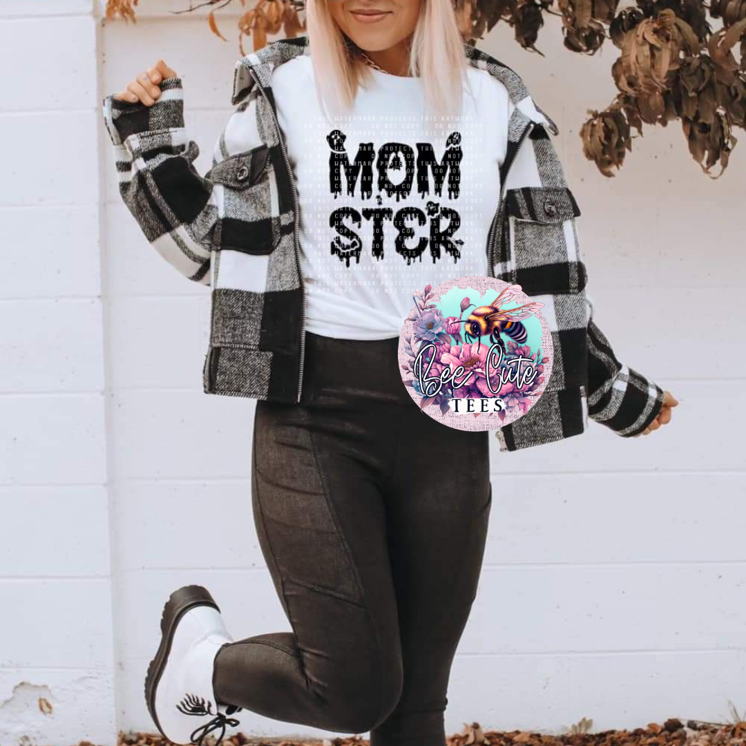 A person wearing a white t-shirt with the text 'Momster' and a logo of a bee, paired with black pants and gray checkered jacket.