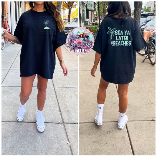 Person wearing a black t-shirt with 'Sea Ya Later Beaches' text and palm tree design on a sidewalk.