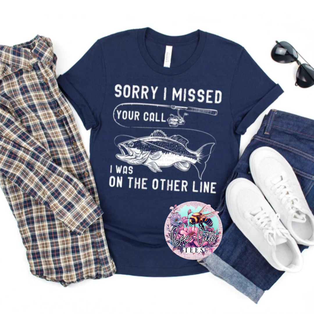 Navy blue t-shirt with fishing graphic and text, plaid shirt, jeans, white sneakers, and sunglasses on a white background.