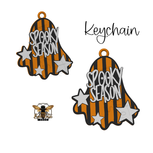 Two ghost-shaped keychain charms with orange and black vertical stripes, white 'SPOOKY SEASON' lettering, and white stars, shown on a white background with the word 'Keychain' and a small bee logo.