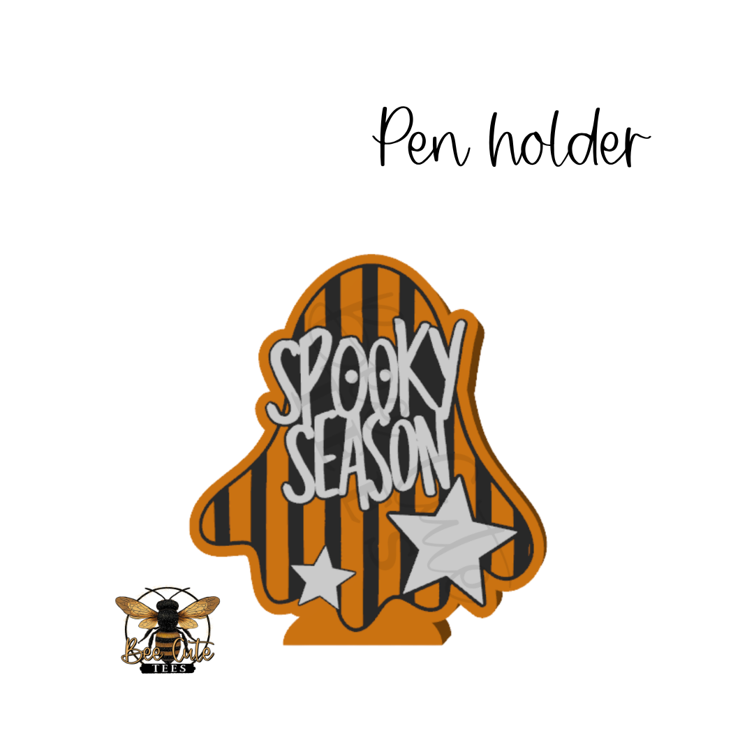 A Halloween-themed ghost-shaped pen holder with black and orange vertical stripes, white 'SPOOKY SEASON' lettering, and two white stars. The image includes the text 'Pen holder' at the top and a bee logo at the bottom left, all on a plain white background.