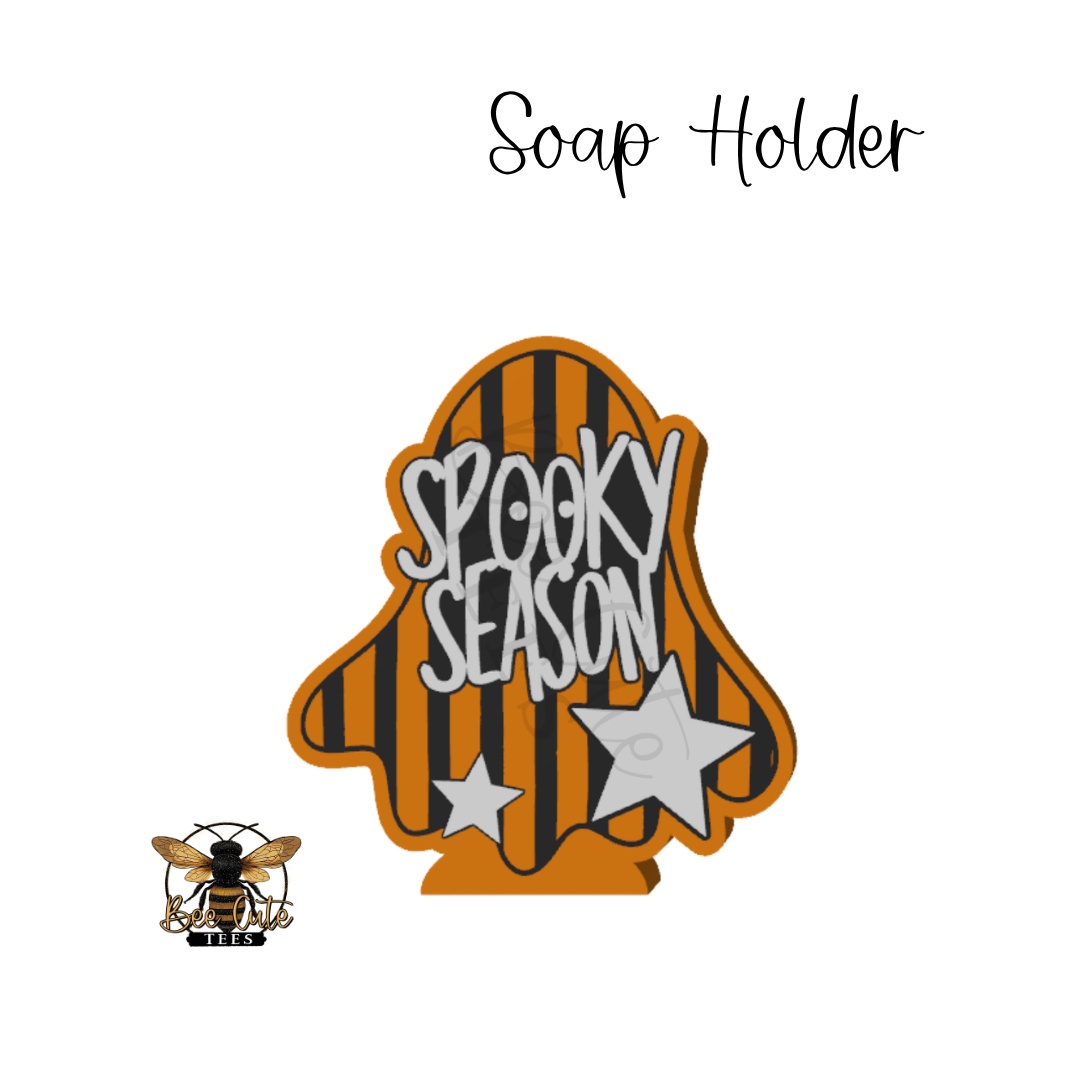 A Halloween-themed ghost-shaped soap holder with orange and black stripes, the words 'SPOOKY SEASON' in white, and two white stars. A small bee logo appears in the lower left, and the text 'Soap Holder' is written at the top on a white background.