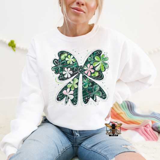 Person wearing a white sweatshirt with a green bow design, sitting on a couch.