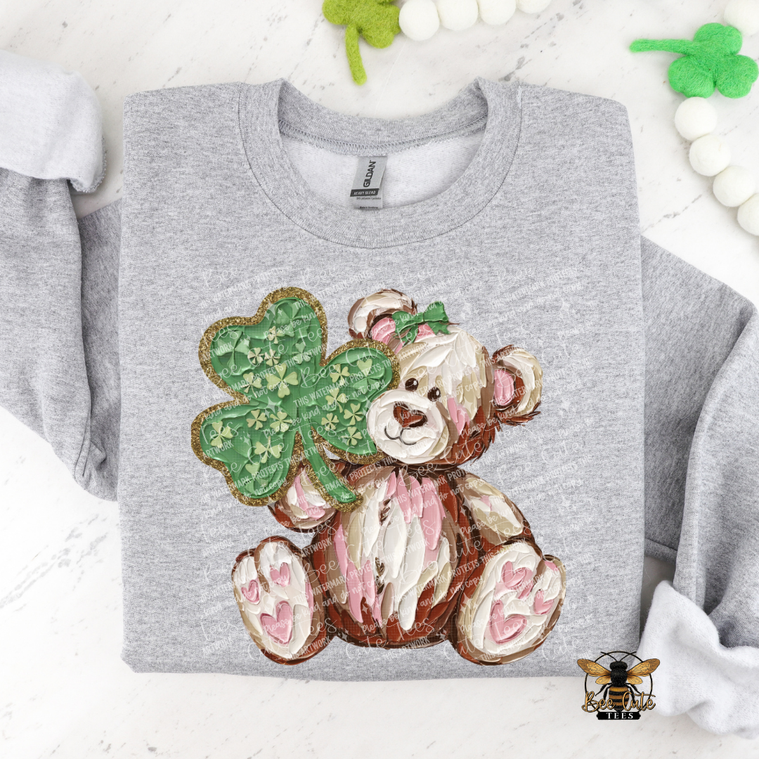 Gray sweatshirt with a teddy bear holding a shamrock design on a white background.