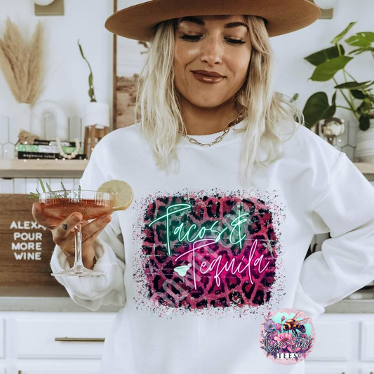 Woman wearing a white sweatshirt with 'Tacos & Tequila' design, holding a drink.