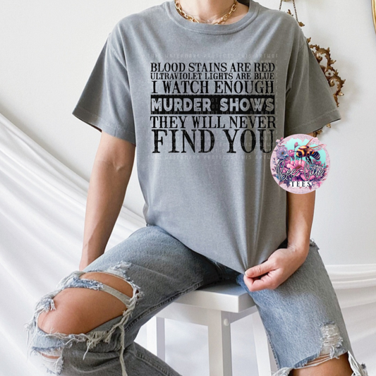 Person wearing a gray t-shirt with a graphic design and ripped jeans sitting on a white stool.