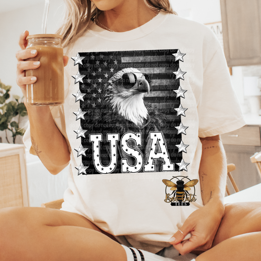 A person holding a drink wearing a white short-sleeve t-shirt with a black and white image of an eagle and the text 'USA' on it.