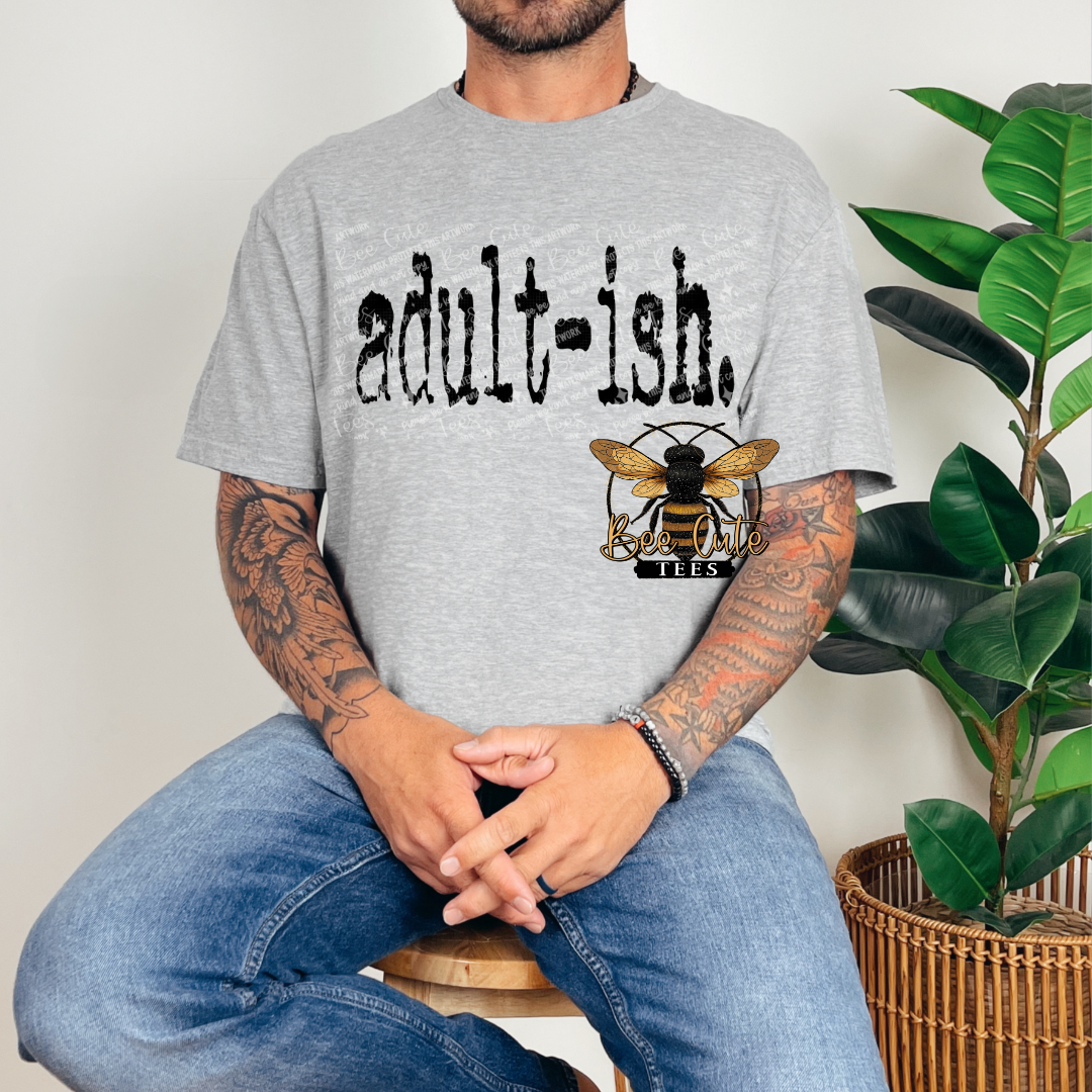 Person wearing a gray t-shirt with 'adult-ish' and a bee logo, sitting next to a plant.