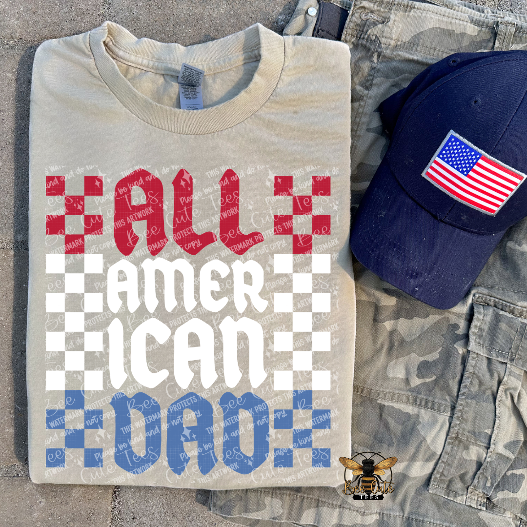 Beige t-shirt with 'All American Dad' text, blue cap with American flag, and camouflage pants on a textured surface.