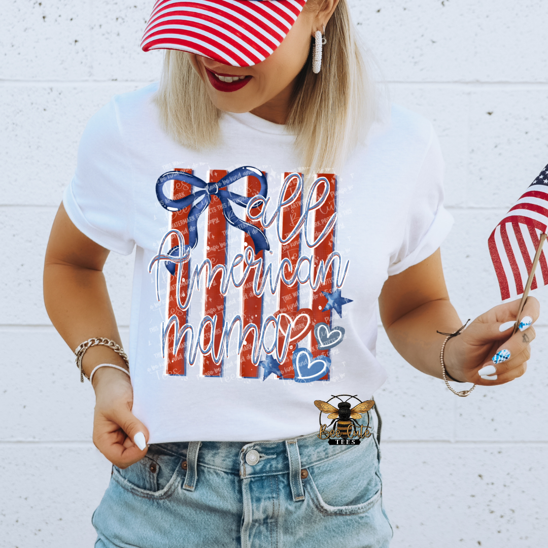 Person wearing a white t-shirt with 'All American Mama' design, holding an American flag, against a white brick wall.