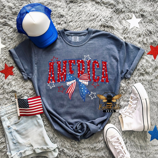 Blue t-shirt with 'AMERICA' print on a gray surface with accessories.