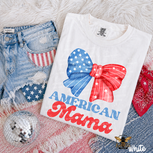 White t-shirt with 'American Mama' design on a textured surface with denim shorts and disco ball.