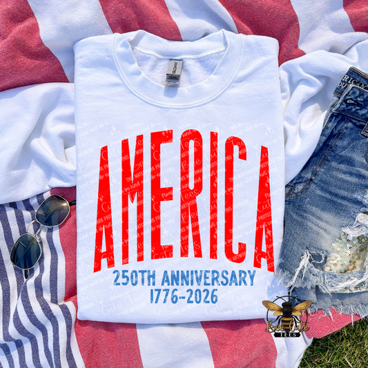 White t-shirt with 'AMERICA 250TH ANNIVERSARY 1776-2026' text on a red, white, and blue striped fabric background.