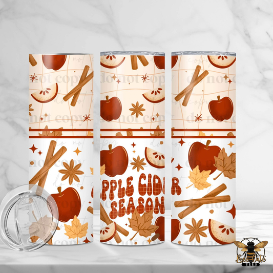 Three insulated tumblers with a fall apple cider season pattern, featuring cinnamon sticks, apples, leaves, and the text 'APPLE CIDER SEASON'. A clear lid is shown in the bottom left on a white marble background.