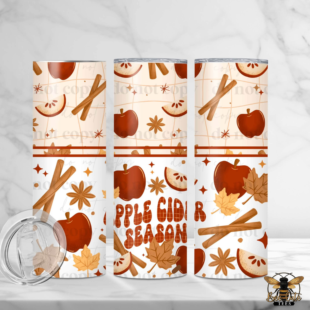 Three insulated tumblers with a fall apple cider season pattern, featuring cinnamon sticks, apples, star anise, and maple leaves on a cream background. The center tumbler displays the text 'APPLE CIDER SEASON' in a rustic orange-brown font.