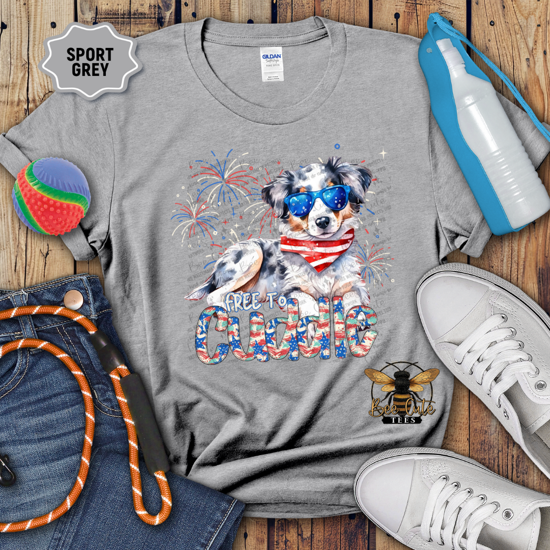 Gray t-shirt with a dog graphic and text, surrounded by jeans, shoes, and sports equipment on a wooden surface.