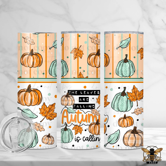 Three insulated tumblers with clear lids are shown on a light marble surface. The tumblers feature an autumn-themed wrap design with pumpkins, leaves, stripes, and the phrase 'The Leaves Are Falling Autumn is calling' in black, white, orange, and teal.