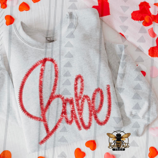 Ash Grey sweatshirt with red 'babe' text and heart shapes on a patterned background