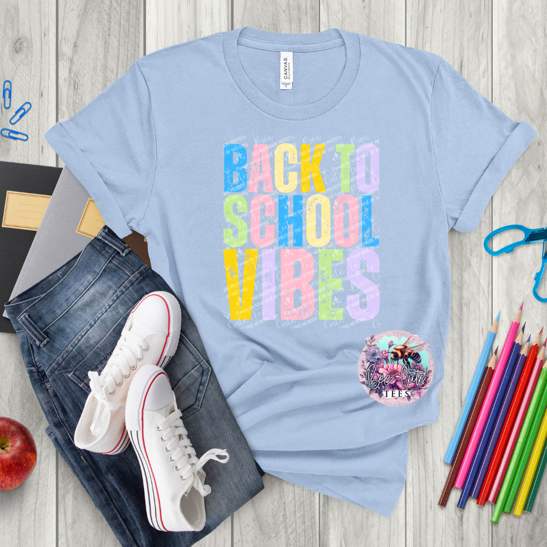 Light blue t-shirt with 'Back to School Vibes' text, jeans, sneakers, and school supplies on a wooden surface.