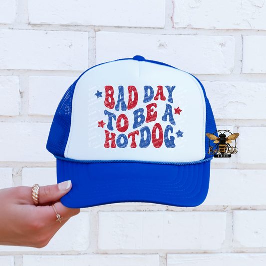 Blue and white cap with 'Bad Day to be a Hotdog' text held against a white brick wall.
