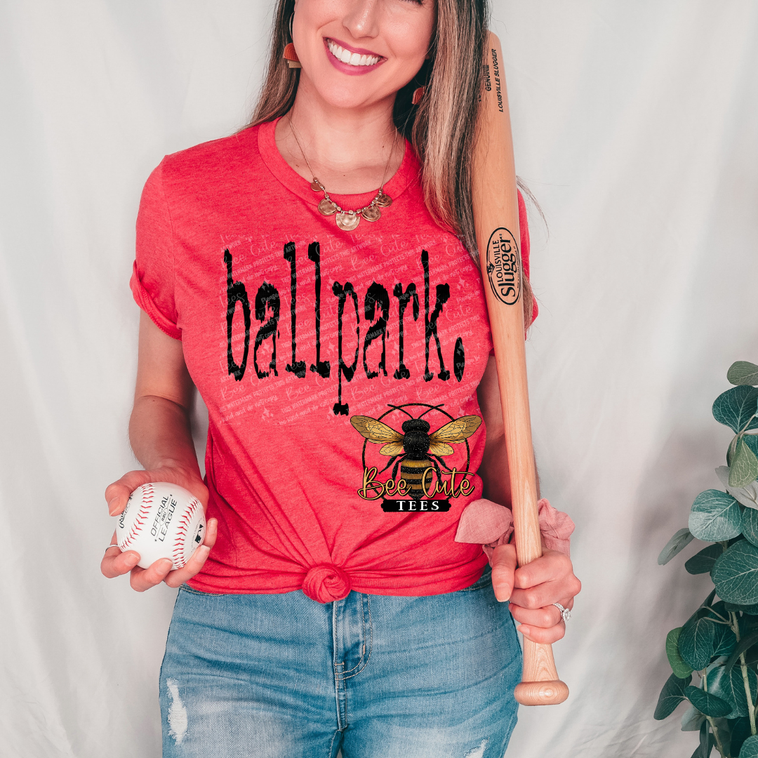 Woman wearing a red 'ballpark' t-shirt holding a baseball and bat against a white background