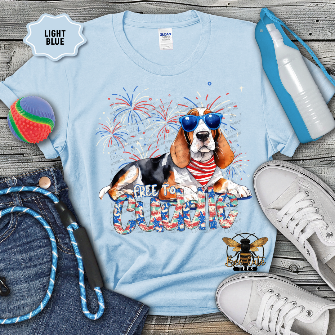 Light blue t-shirt with a dog graphic and 'Free to Cuddle' text, surrounded by accessories on a wooden surface.