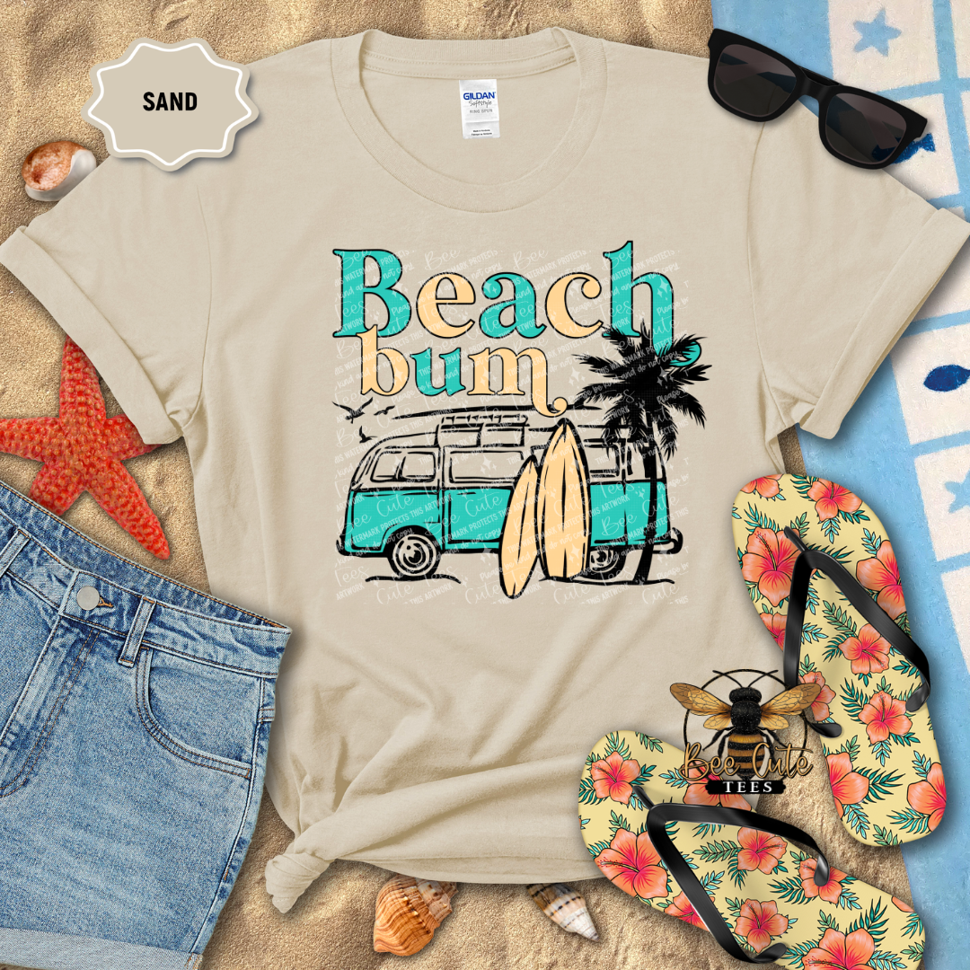 Beach-themed t-shirt with 'Beach bum' text, van, and surfboards, surrounded by beach accessories on sand.