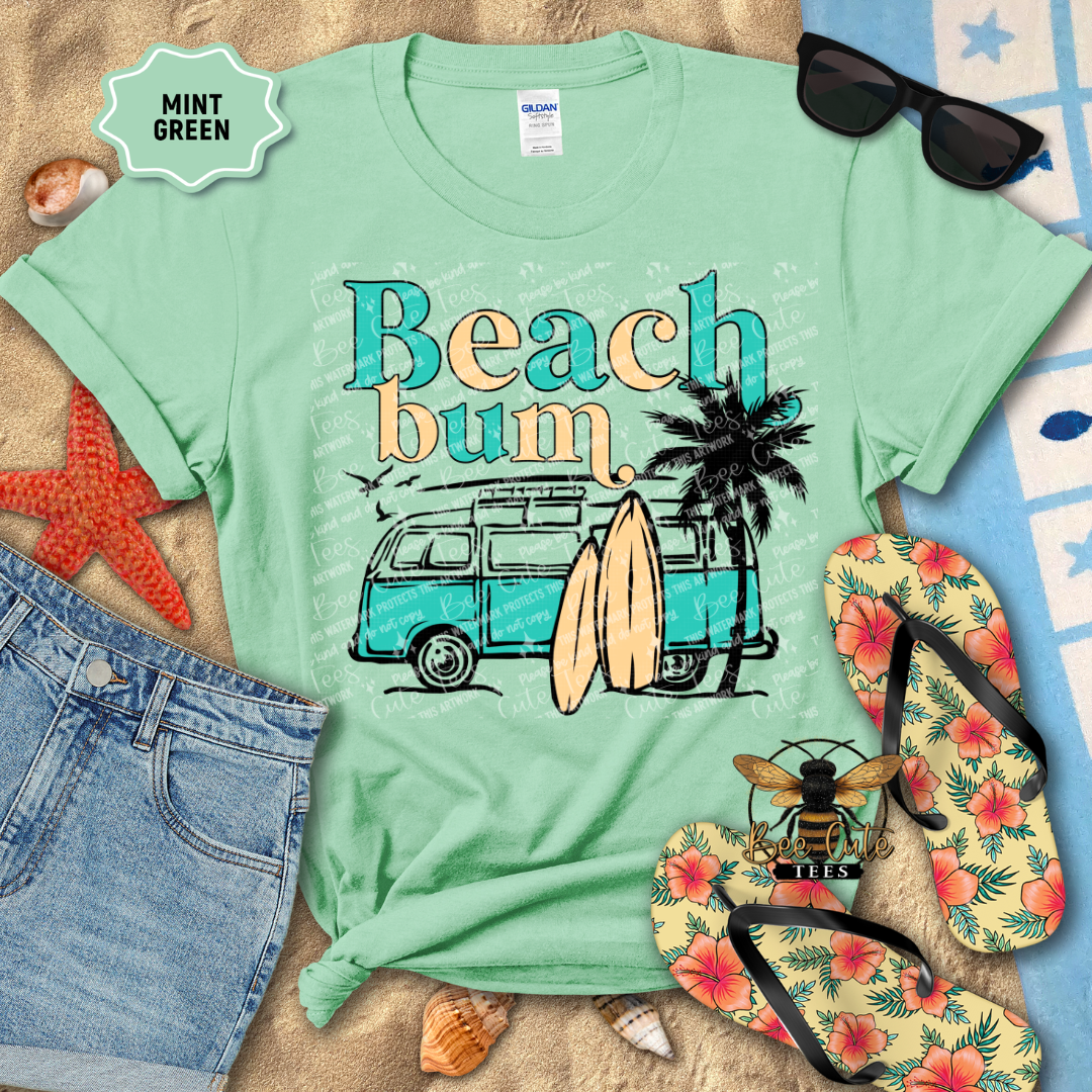 Mint green t-shirt with 'Beach bum' graphic on a sandy background with flip-flops and sunglasses.