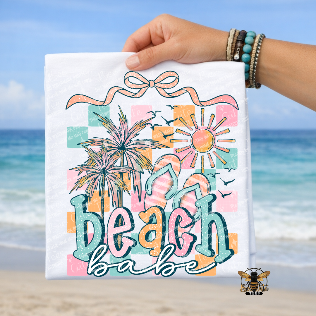 Hand holding a white t-shirt with 'Beach Babe' design against a beach background