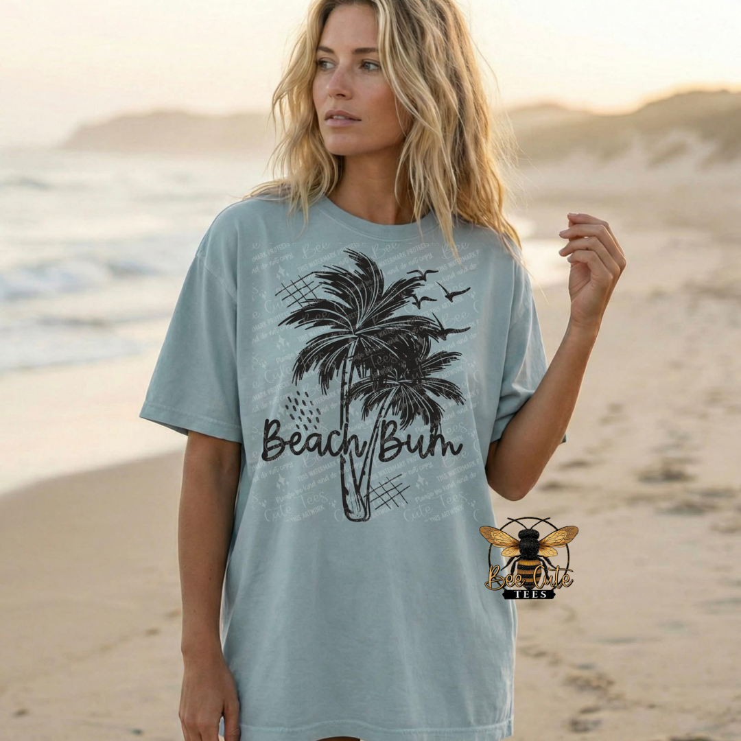 Woman wearing a light blue t-shirt with a palm tree design and 'Beach Bum' text on a beach.
