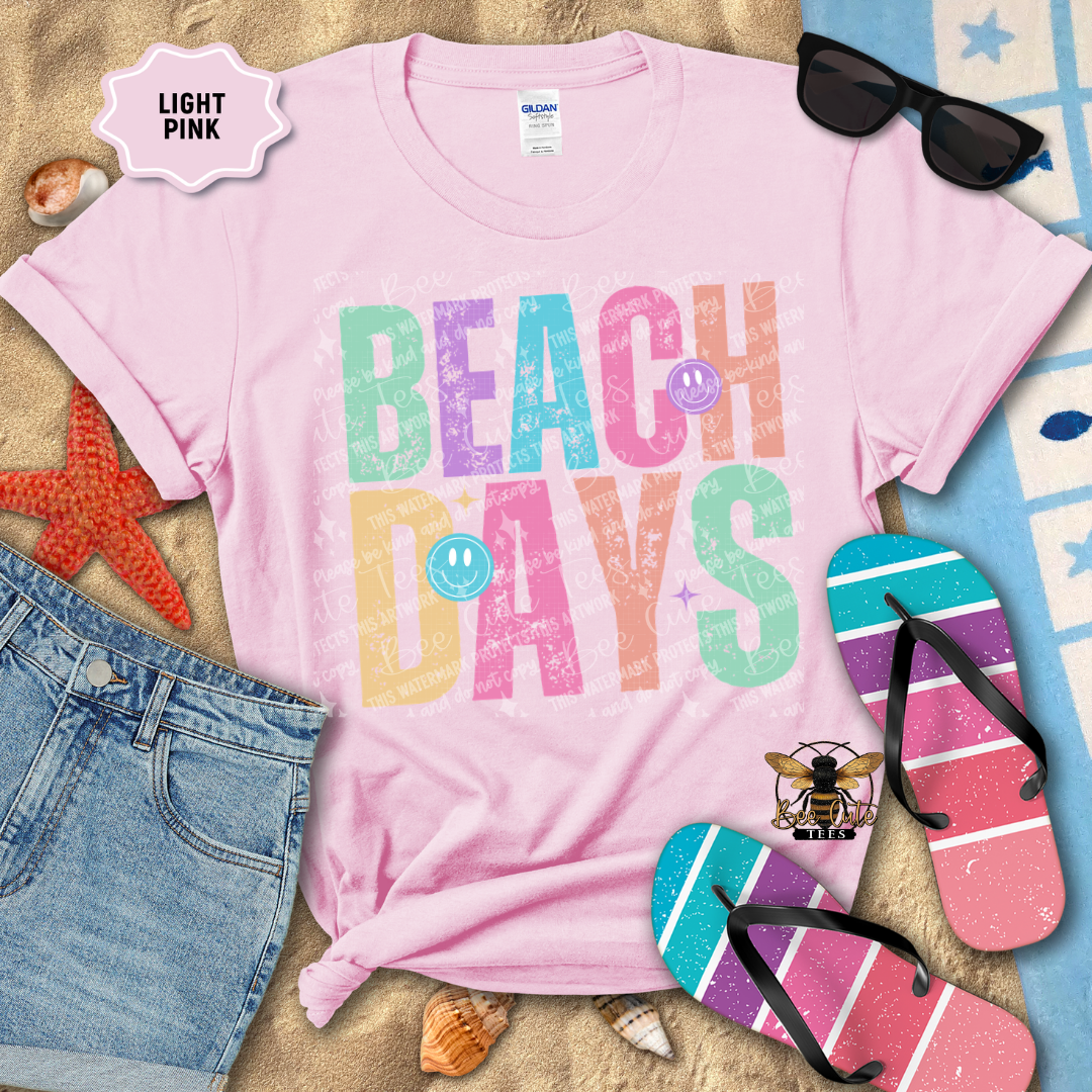 Light pink t-shirt with 'Beach Days' text, sunglasses, flip-flops, and beach accessories on a sandy background.