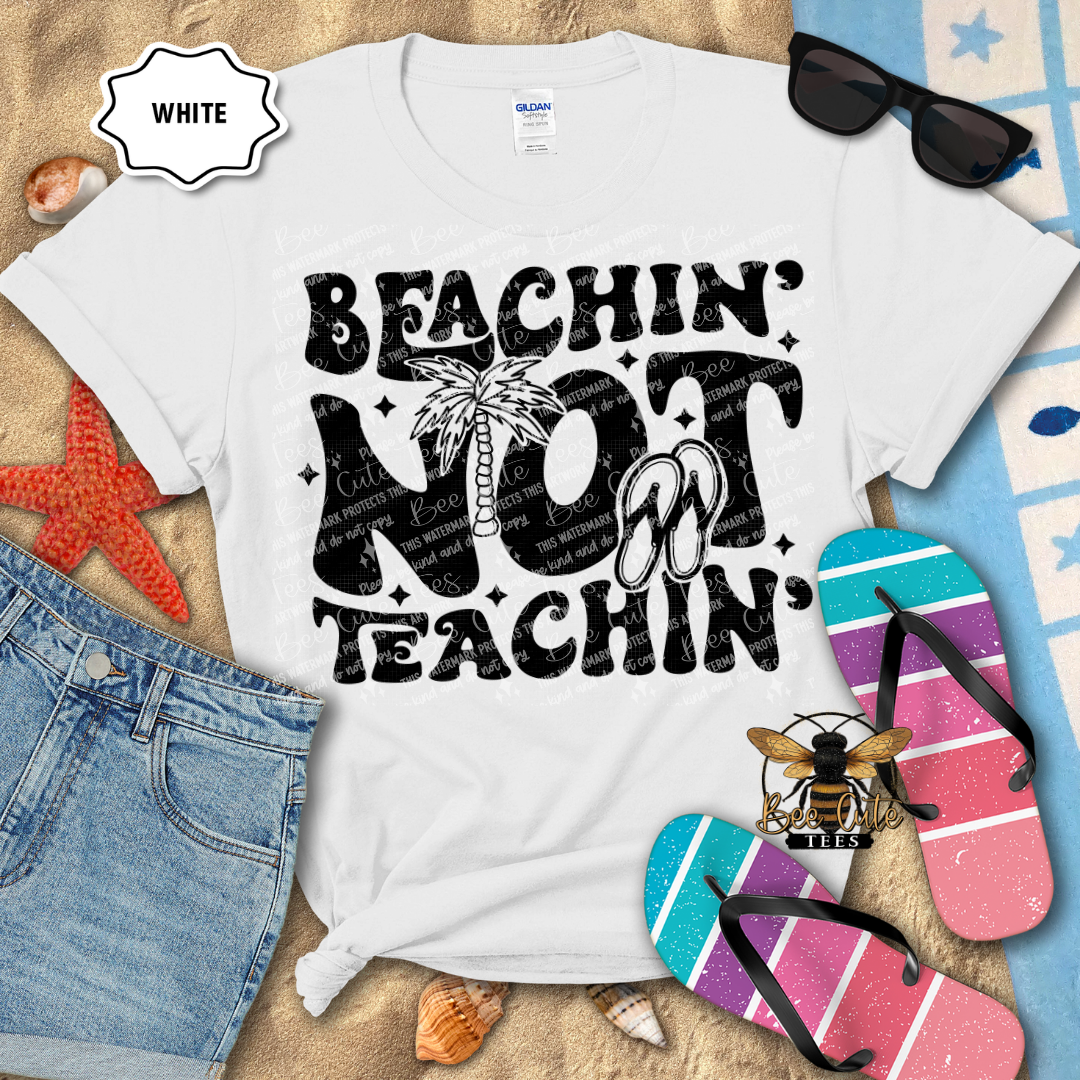 White t-shirt with 'Beachin' Not Teachin' design on a beach-themed background with flip-flops and sunglasses.