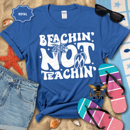 Blue t-shirt with 'Beachin' Not Teachin' design, sunglasses, and flip-flops on a beach-themed background.