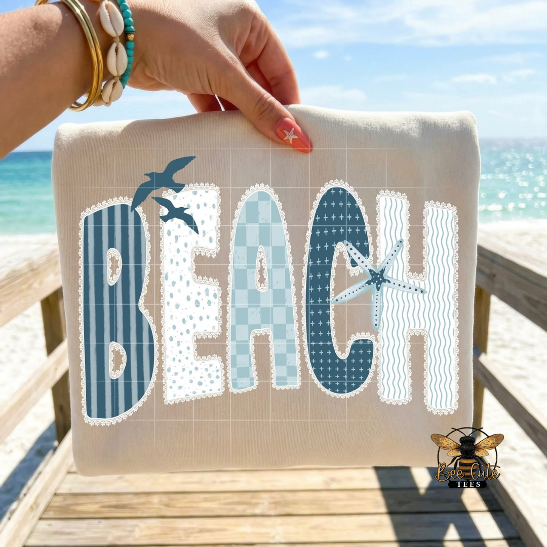 Hand holding a beige t-shirt with 'BEACH' text against a beach background