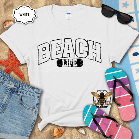 White t-shirt with 'BEACH LIFE' text, sunglasses, and flip-flops on a sandy background