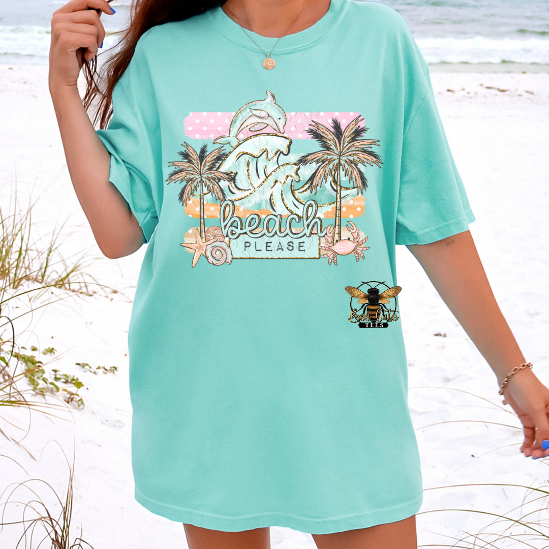 Person wearing a light green t-shirt with beach-themed graphics on a beach.