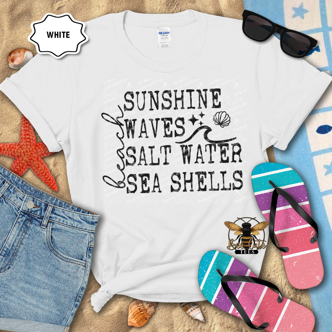 White t-shirt with beach-themed text on a sandy background with flip-flops and sunglasses.