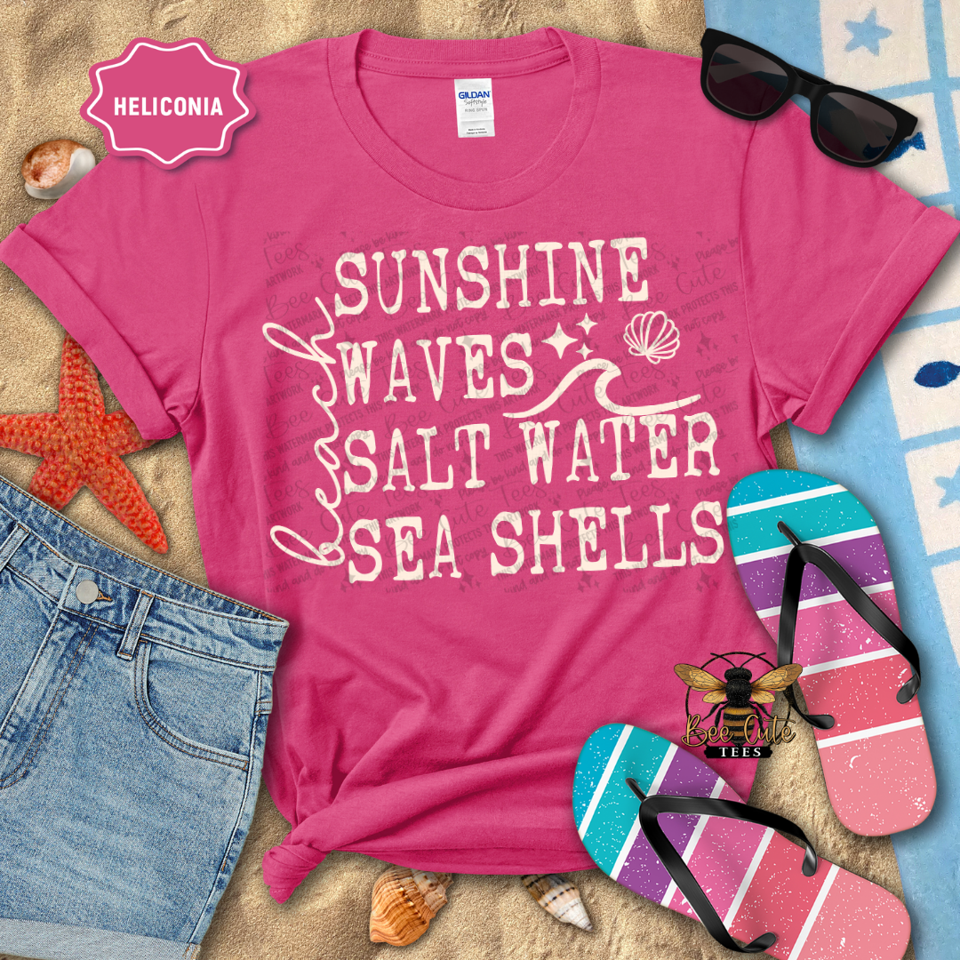 Pink t-shirt with beach-themed text on a sandy background with flip-flops and sunglasses.