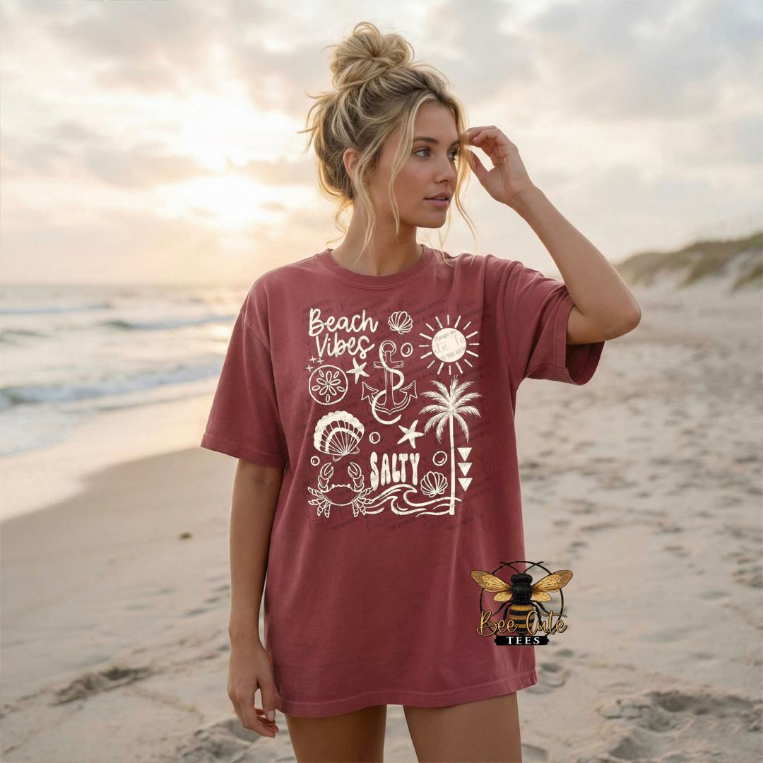 Woman wearing a red t-shirt with beach-themed graphics on a beach.