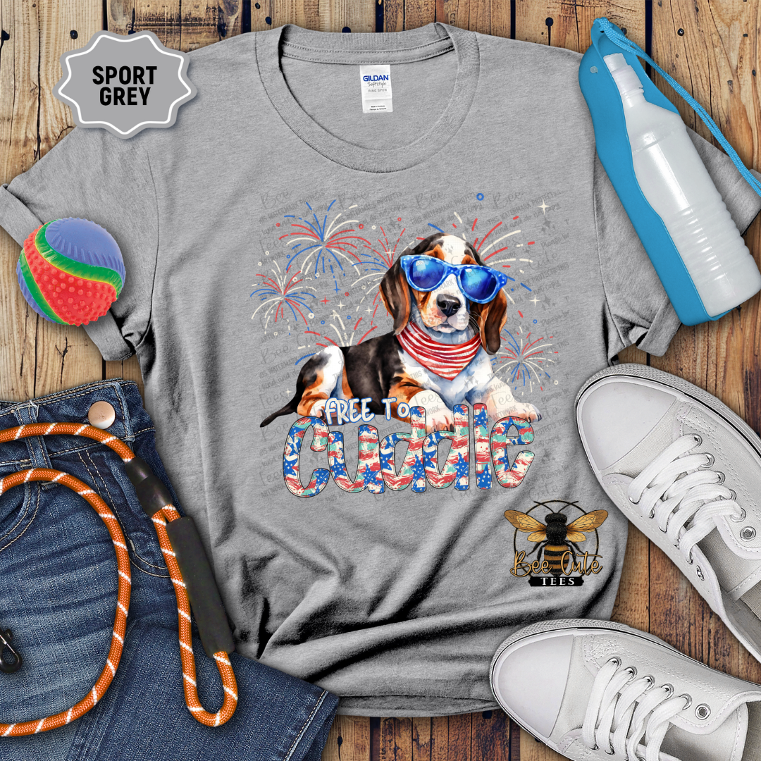 Gray t-shirt with a dog graphic and 'Free to Cuddle' text on a wooden surface with accessories.